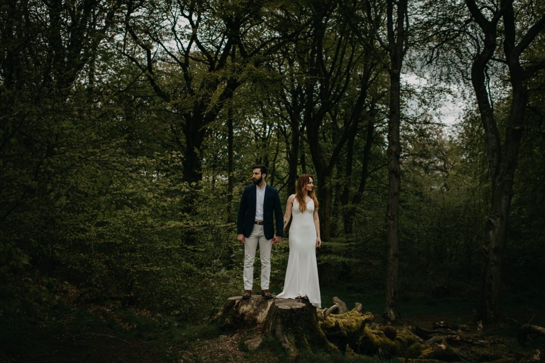 Couple standing on log in Scottish forest whilst eloping in Scottish Highlands