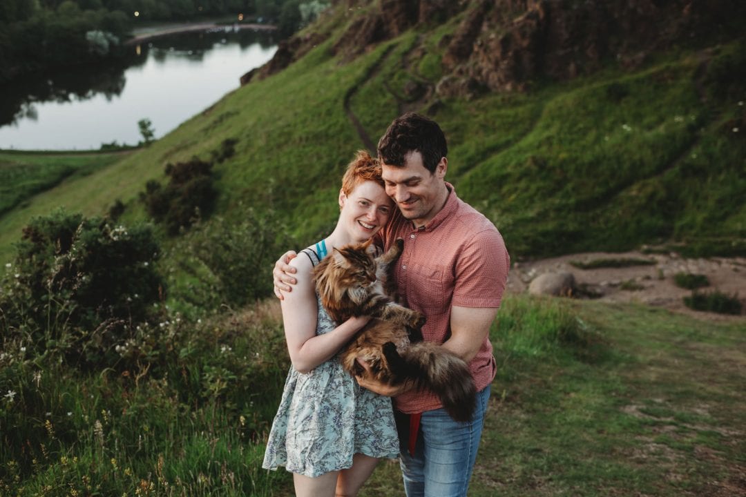 happy couple hiking with mainecoon cat during couples photoshoot in Edinburgh - Holyrood Park