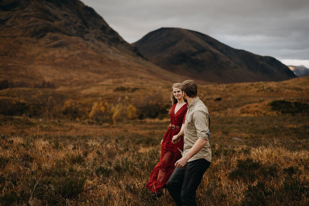 Couple snuggled together next to Buachaille Etive Mòr in Scottish Highlands mountain scenery during photo adventure session