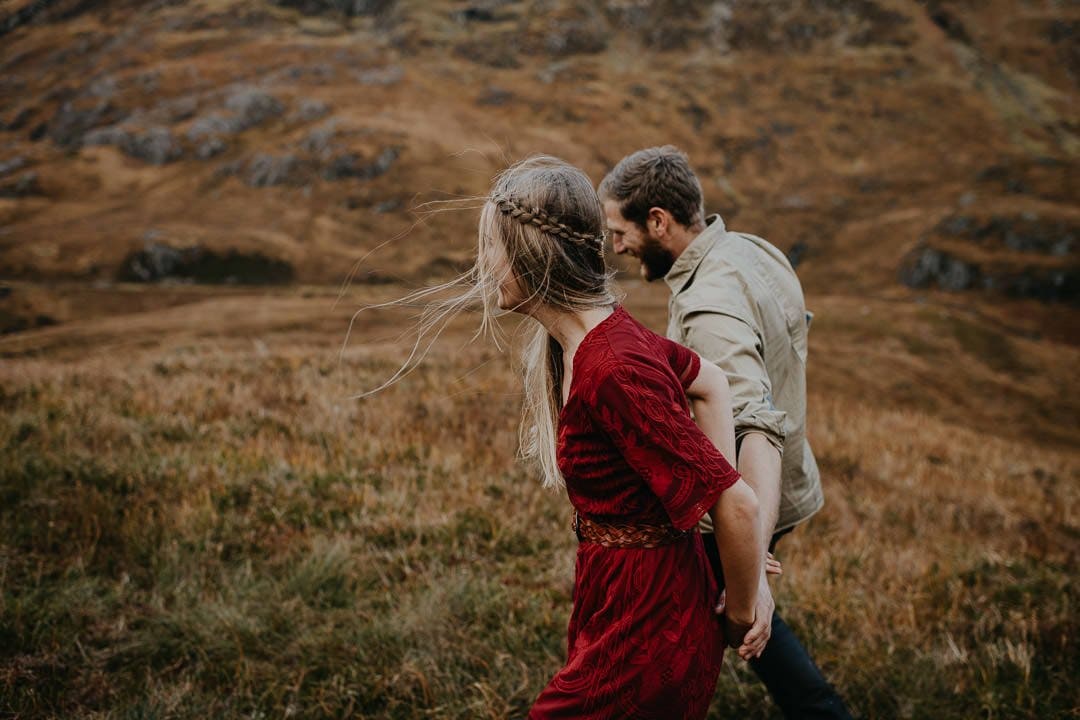 Couple walking through glen during adventure session in Glencoe, Scottish Highlands