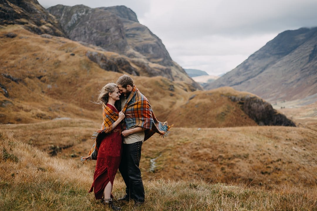 Windy elopement romantic photoshoot in Glencoe, Scottish Highlands wearing a tartan blanket