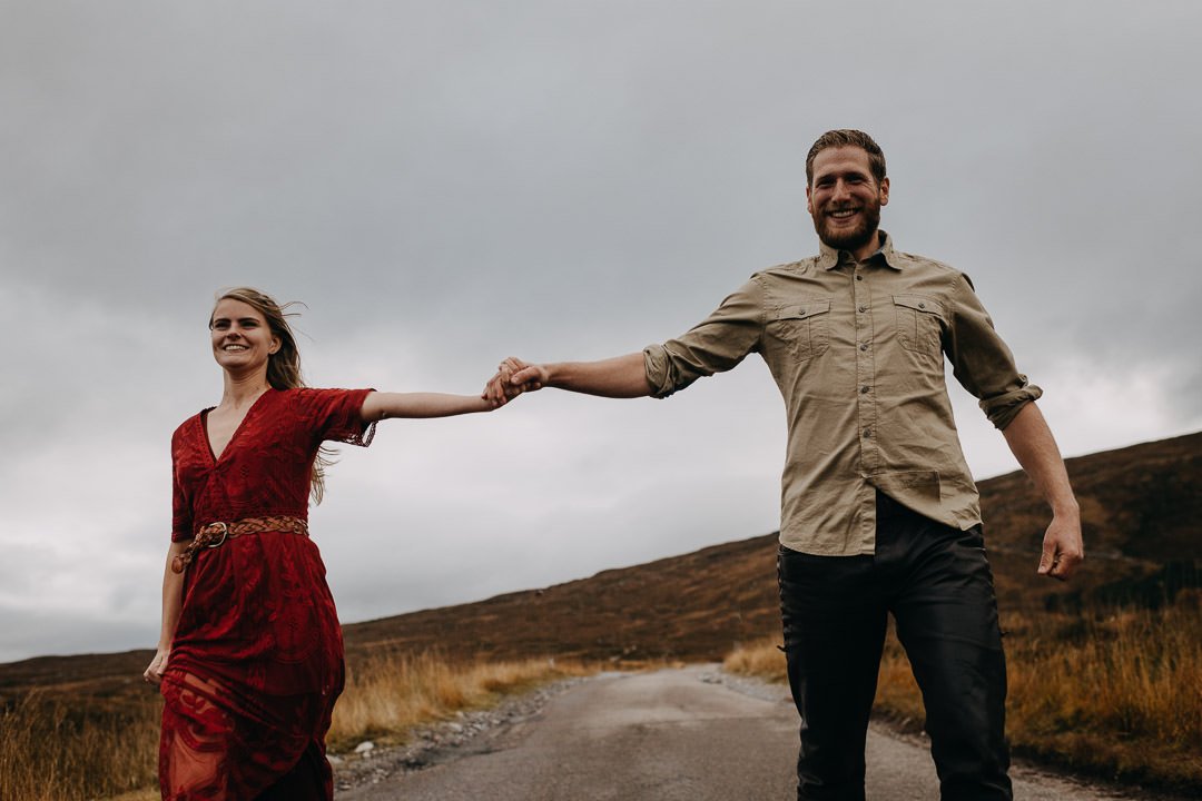 Gleeful couple running through the Scottish Highlands on an adventure photoshoot