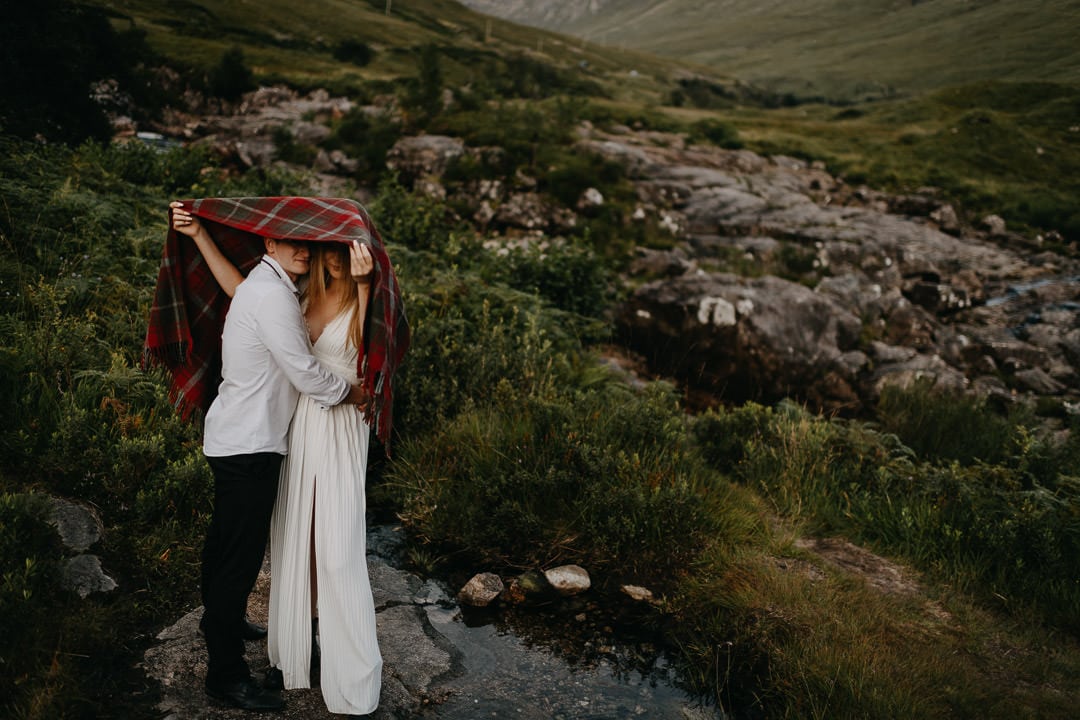 Elopement couple hiding under Tartan Blanket Co blanket from midges during Glen Etive elopement
