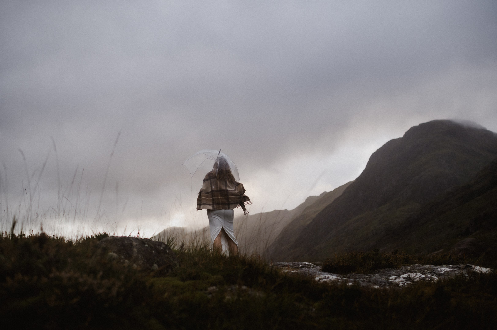 Bride climbing hill with umbrella during stormy Glencoe elopement