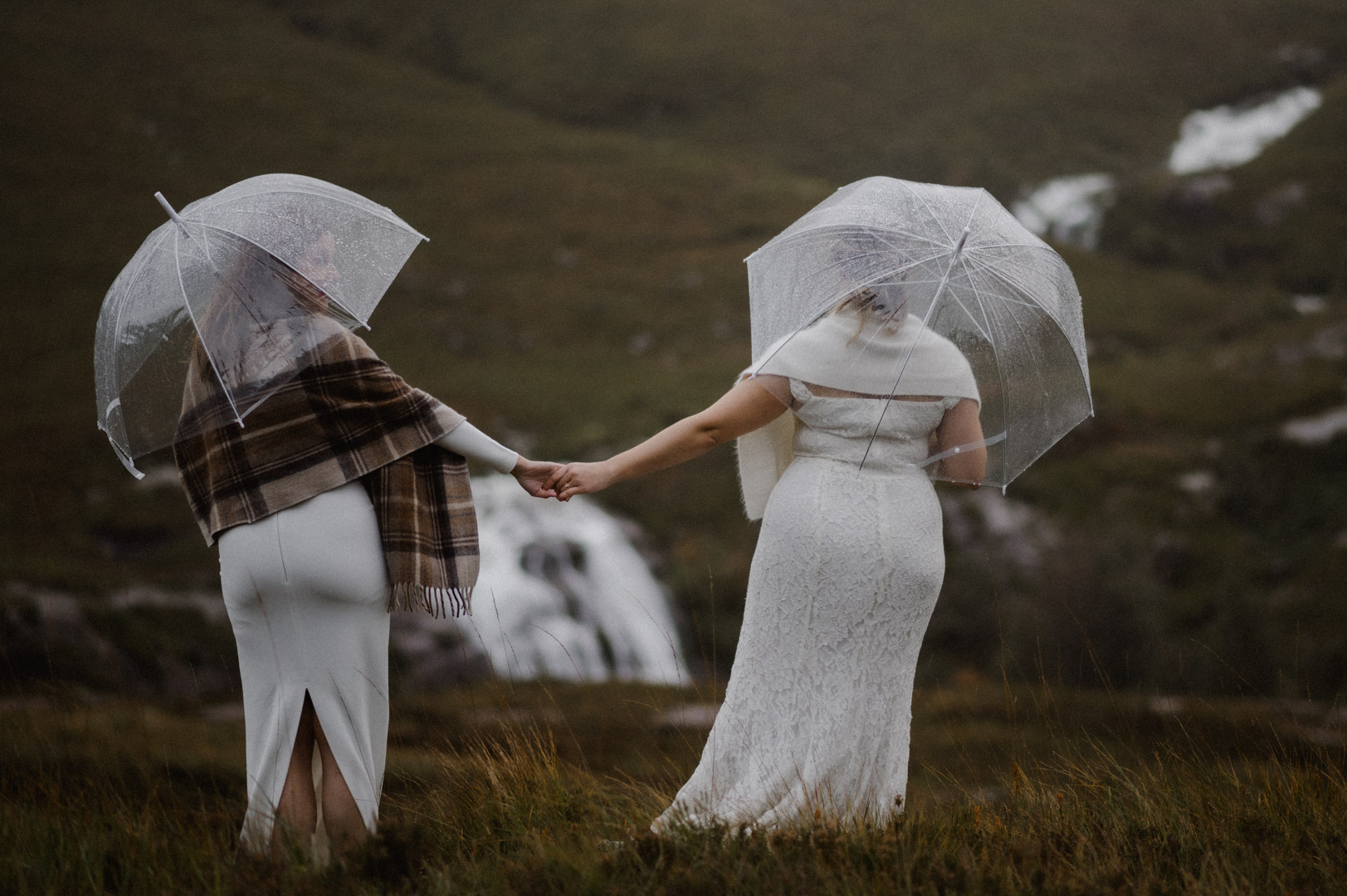 Two brides holding umbrellas in Glencoe by waterfalls