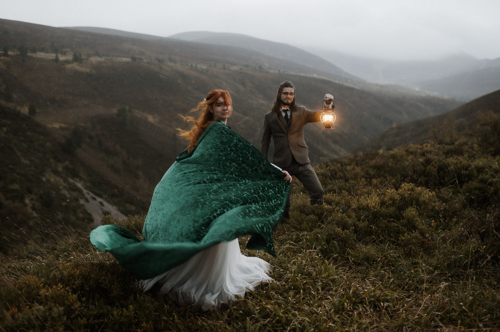 Bride wearing a cloak in the rain of scottish elopement - groom holding a lantern in a romantic fairytale way