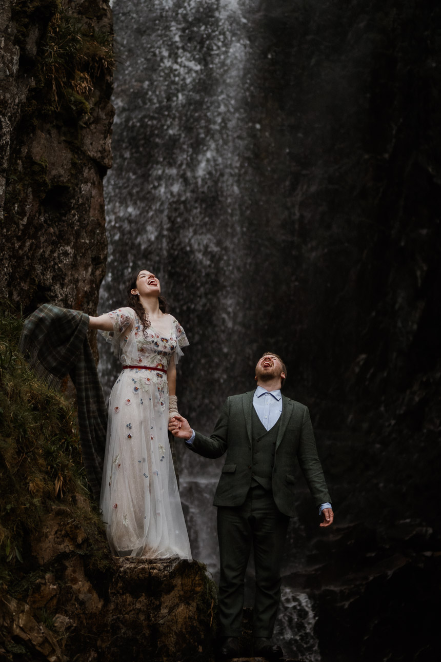 Couple with tongues out underneath waterfall during Scottish elopement