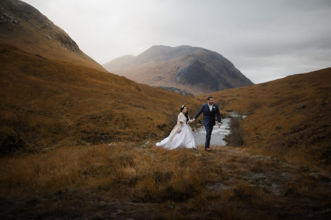 Glen etive elopement in Autumn - couple walking along grass with hills in the background