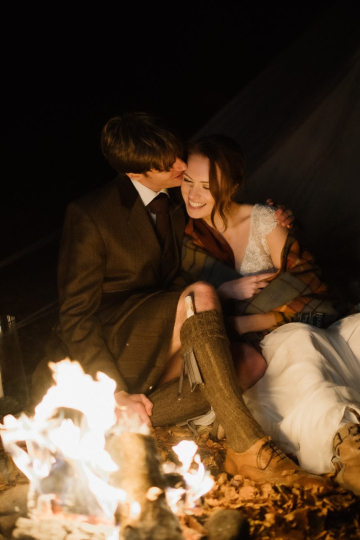 Couple snuggling up by campfire during Scottish elopement